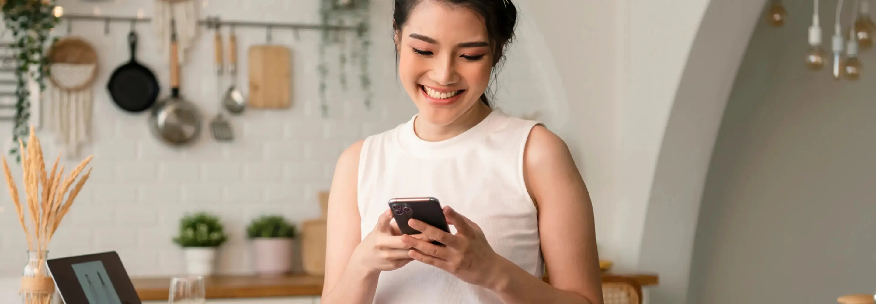 Lifestyle Moment - Woman Smiling at Phone: A happy resident in her Hillhaven kitchen, smiling as she reads on her phone, showcasing the warm and community-oriented lifestyle at Hillhaven.
